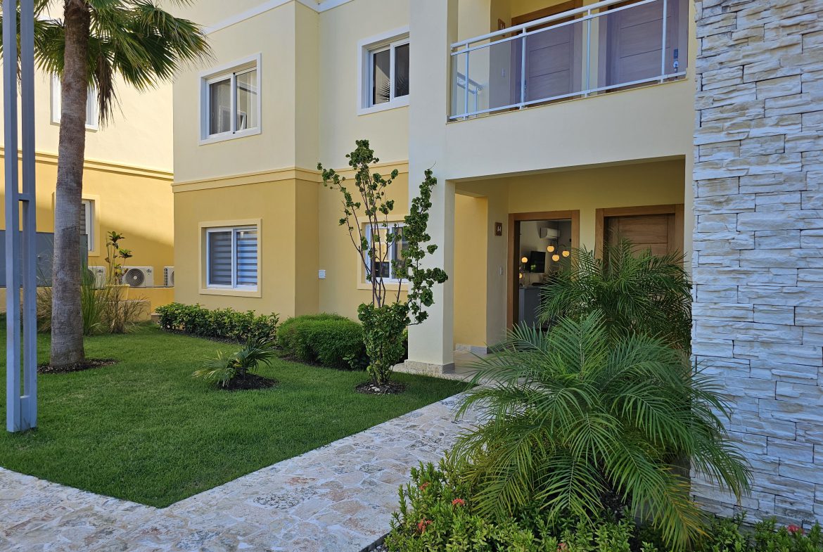 buyDRproperty Exterior of a modern yellow apartment building with lush green lawn and stone walkway. Sosua Real Estate