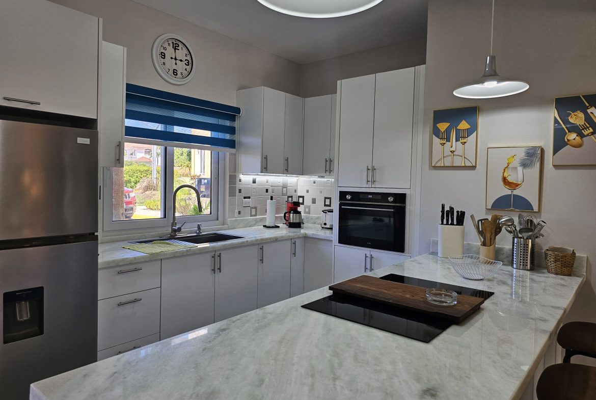 buyDRproperty Modern kitchen with white cabinets, marble countertops, stainless steel fridge, and blue striped blinds. Sosua Real Estate