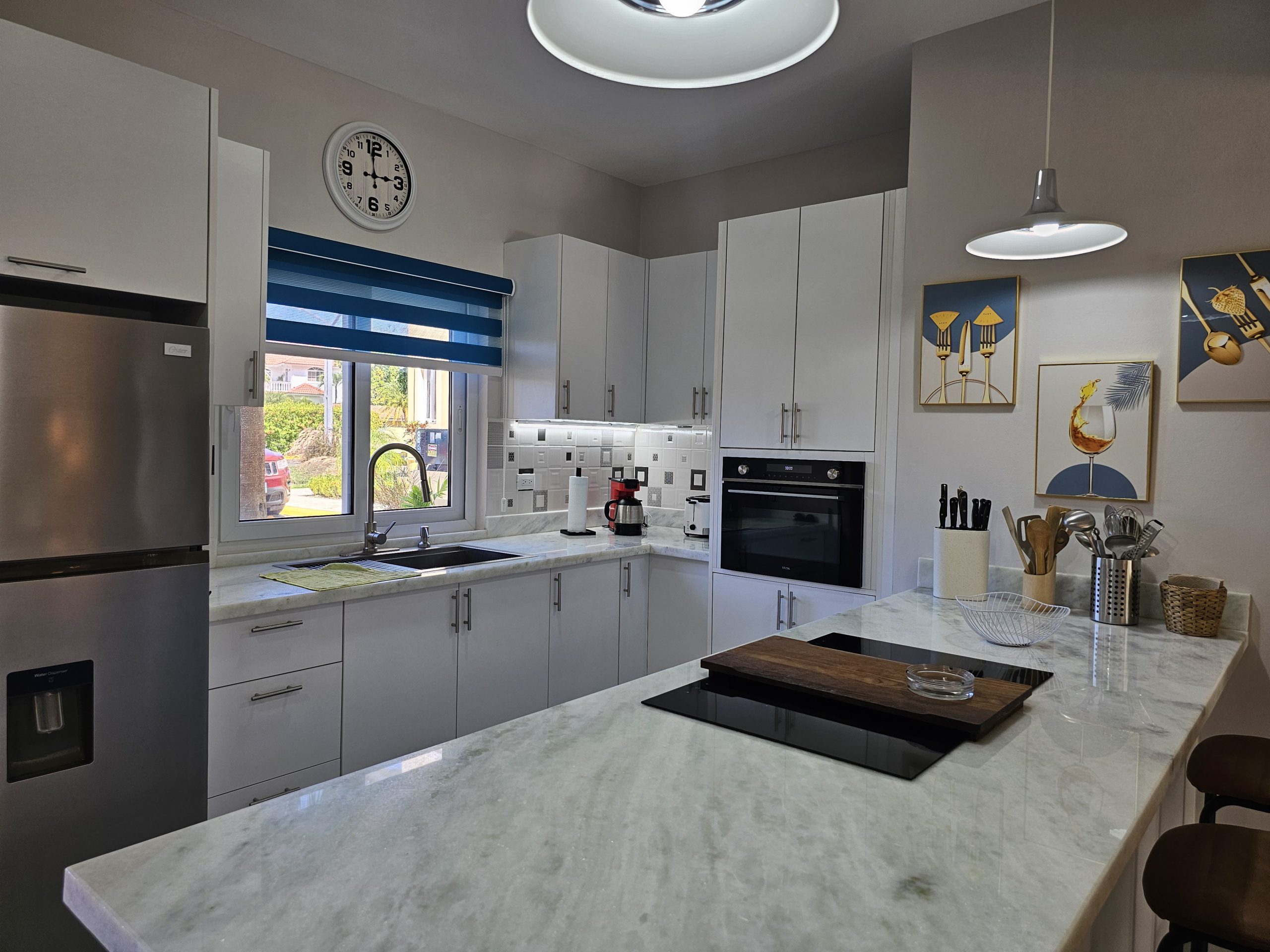 buyDRproperty Modern kitchen with white cabinets, marble countertops, stainless steel fridge, and blue striped blinds. Sosua Real Estate