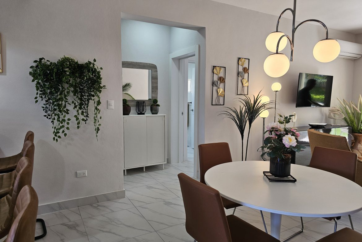buyDRproperty Bright, modern dining area with white table, brown chairs, stylish lighting, and decorative wall accents. Sosua Real Estate