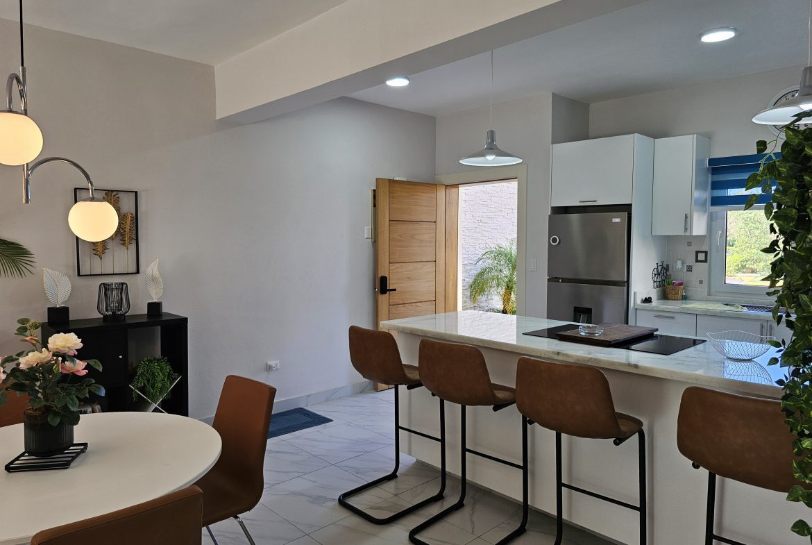 buyDRproperty Modern kitchen with island, bar stools, dining table, and sleek appliances. Bright, open concept design. Sosua Real Estate