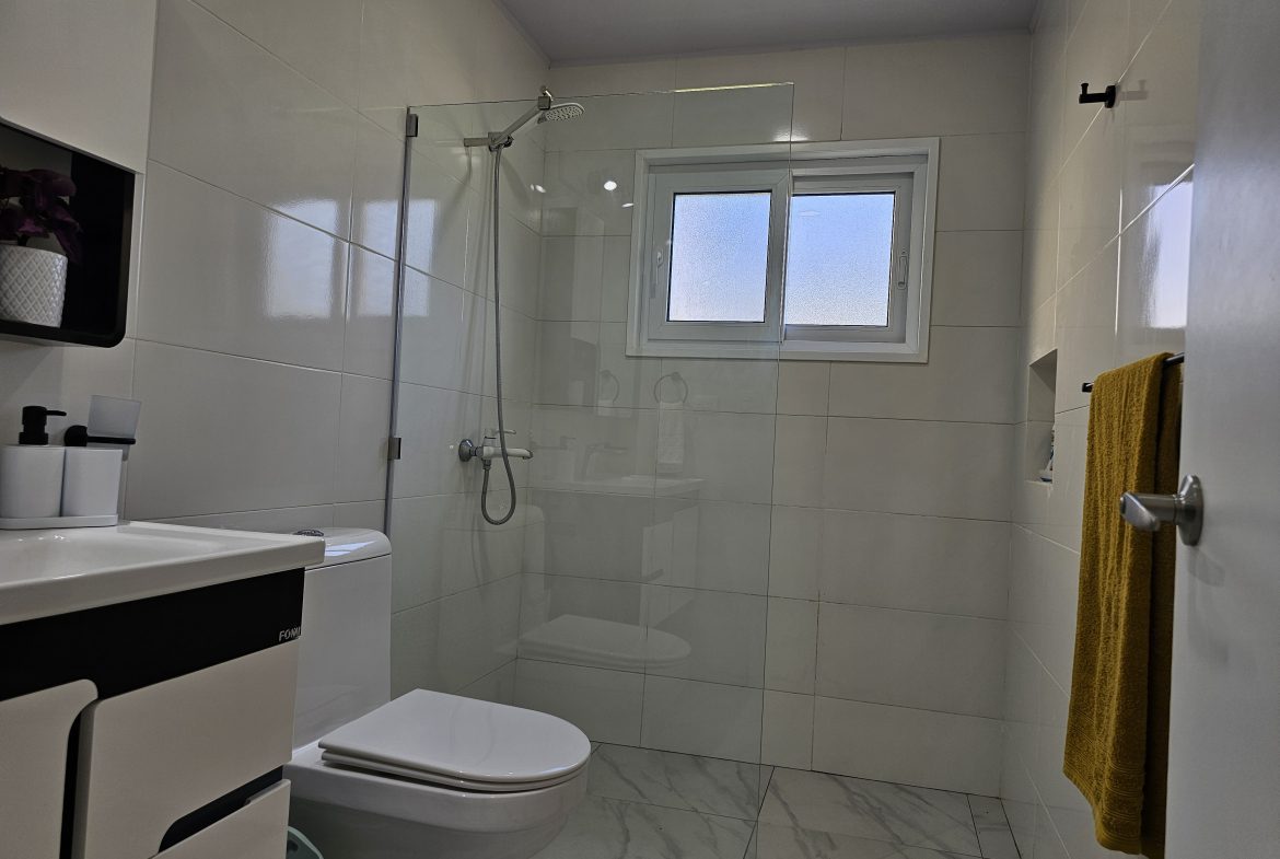 buyDRproperty Modern bathroom with glass shower, toilet, sink, and marble floor. Sosua Real Estate