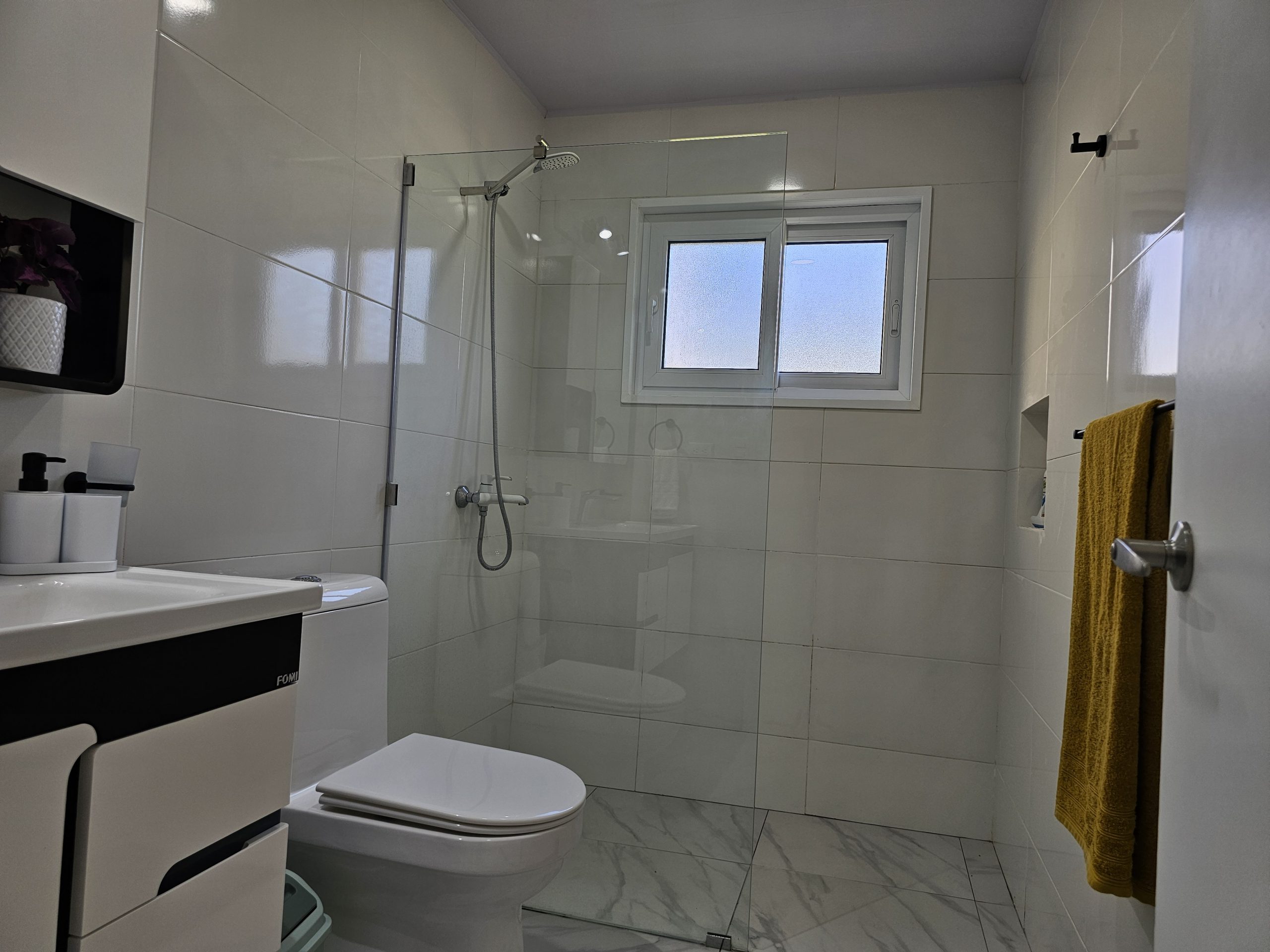 buyDRproperty Modern bathroom with glass shower, toilet, sink, and marble floor. Sosua Real Estate