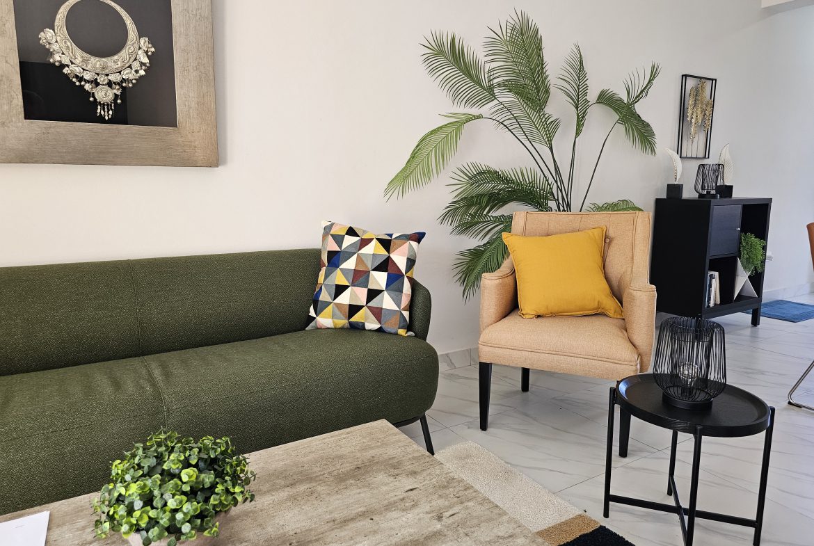 buyDRproperty Stylish living room with green sofa, peach armchair, palm plant, and modern decor on a marble floor. Sosua Real Estate