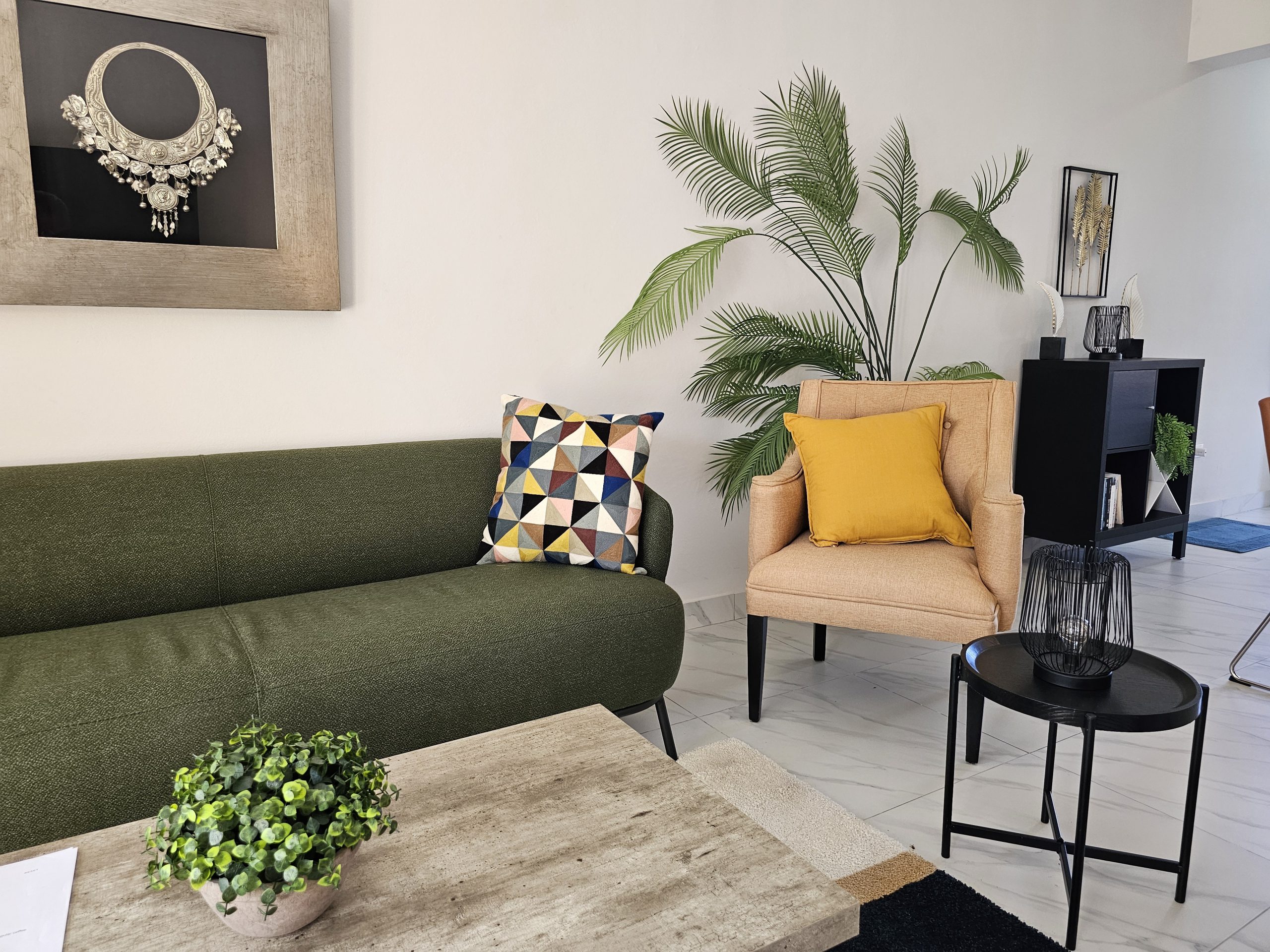 buyDRproperty Stylish living room with green sofa, peach armchair, palm plant, and modern decor on a marble floor. Sosua Real Estate