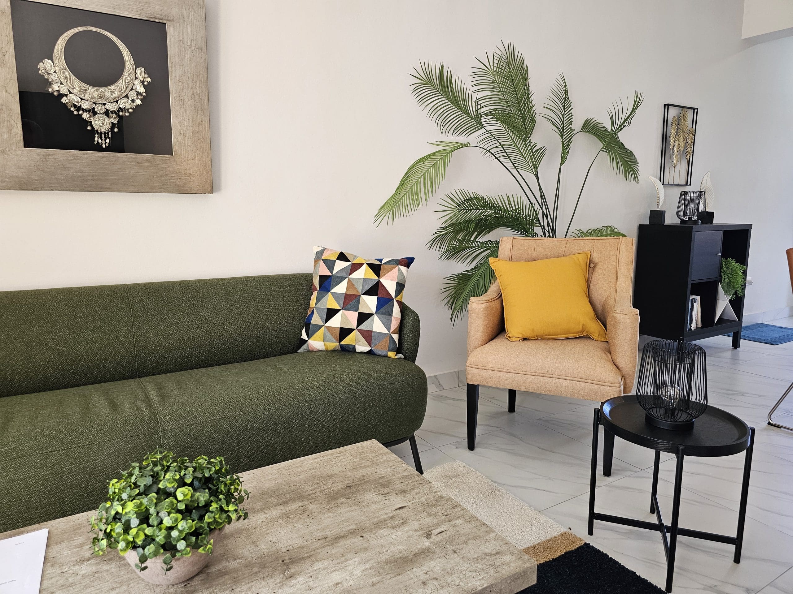 buyDRproperty Stylish living room with green sofa, peach armchair, palm plant, and modern decor on a marble floor. Sosua Real Estate