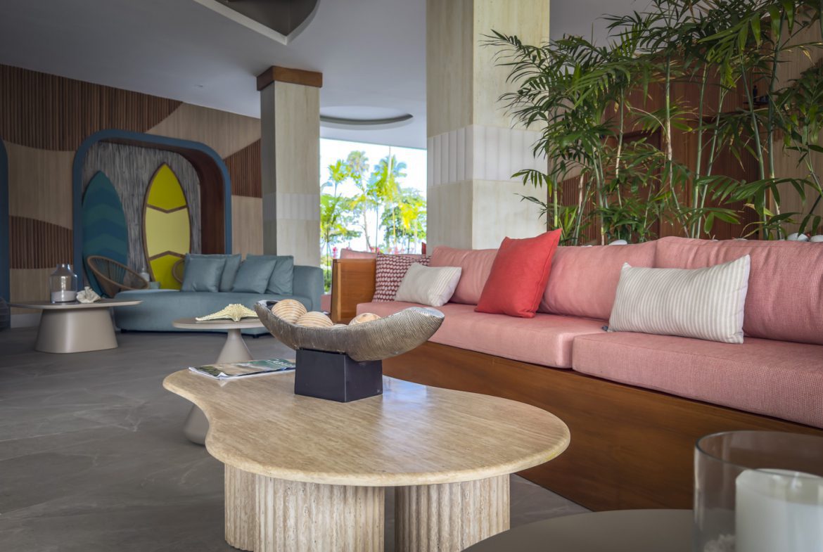 buyDRproperty Stylish hotel lobby with colorful sofas, surfboard art, and tropical plants. Modern resort interior design. Sosua Real Estate