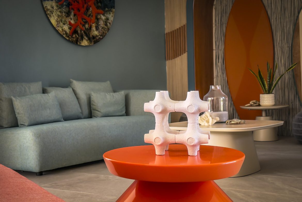 buyDRproperty Modern living room with blue sofa, orange table, and surfboard decor. Coastal interior design. Sosua Real Estate