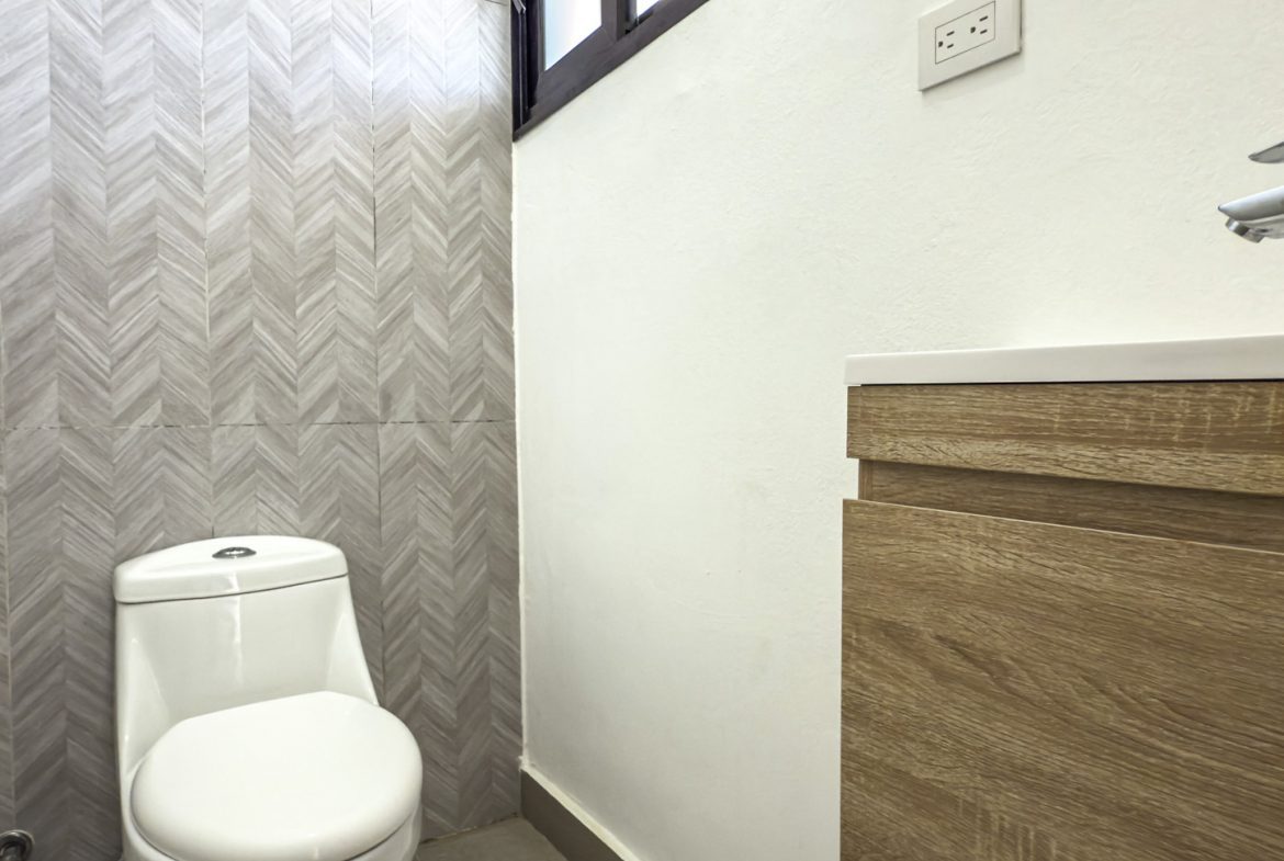 buyDRproperty Modern bathroom with white toilet, wood vanity, chevron tile wall, and electrical outlet. Sosua Real Estate