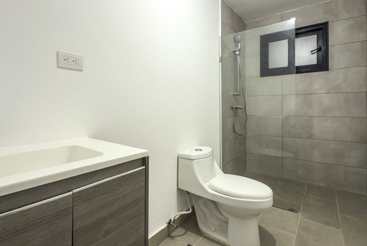 buyDRproperty Modern bathroom with white toilet, gray tiled shower, and vanity with a sleek sink and faucet. Sosua Real Estate