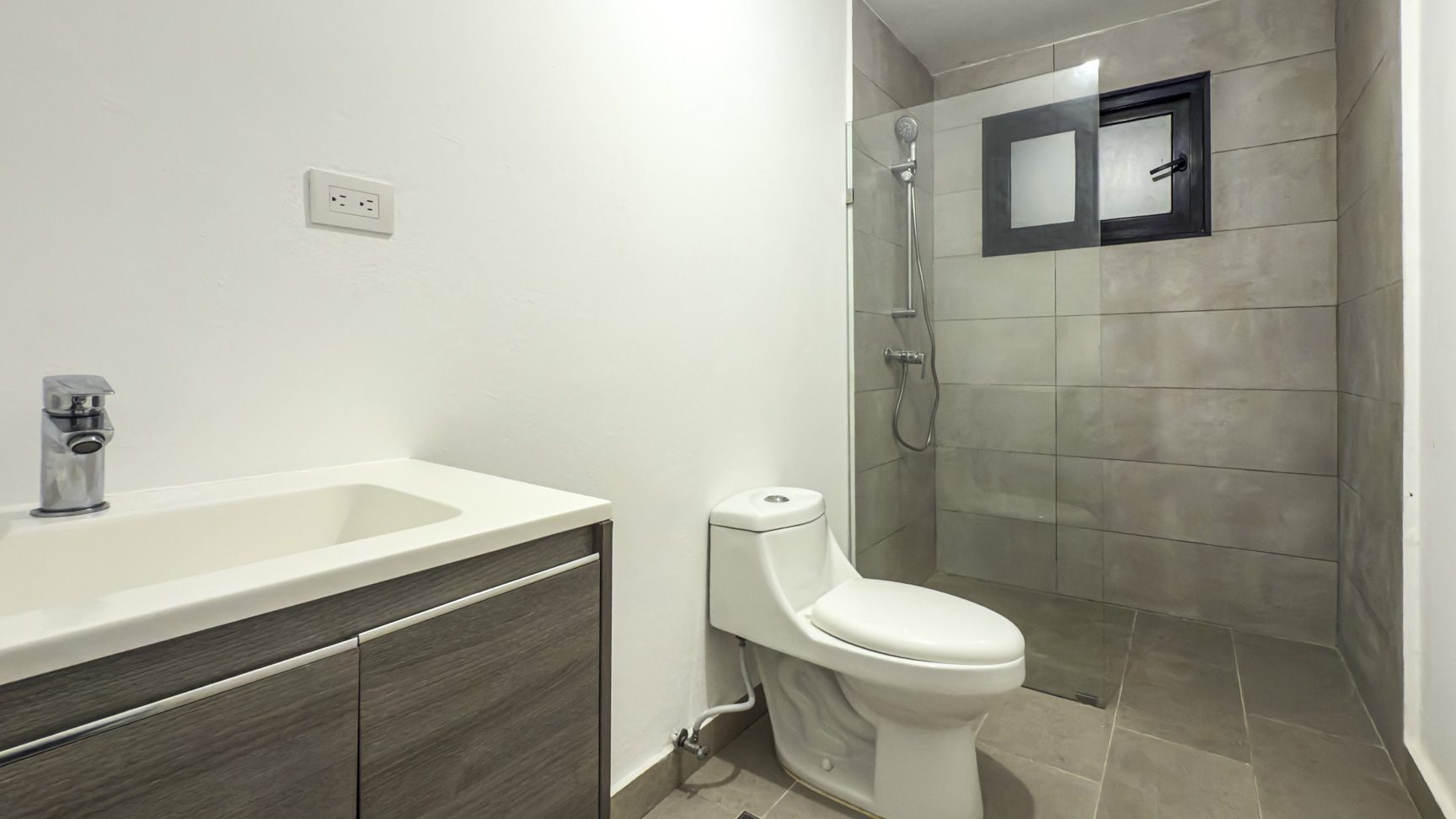 buyDRproperty Modern bathroom with white toilet, gray tiled shower, and vanity with a sleek sink and faucet. Sosua Real Estate