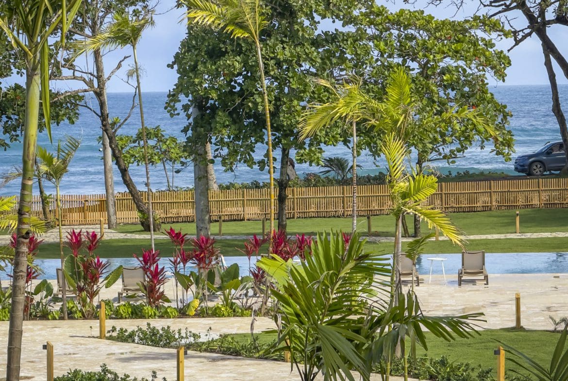 buyDRproperty Tropical resort pool with lounge chairs, palm trees, and ocean view. Sosua Real Estate