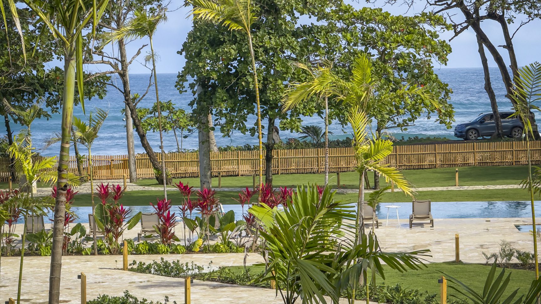 buyDRproperty Tropical resort pool with lounge chairs, palm trees, and ocean view. Sosua Real Estate