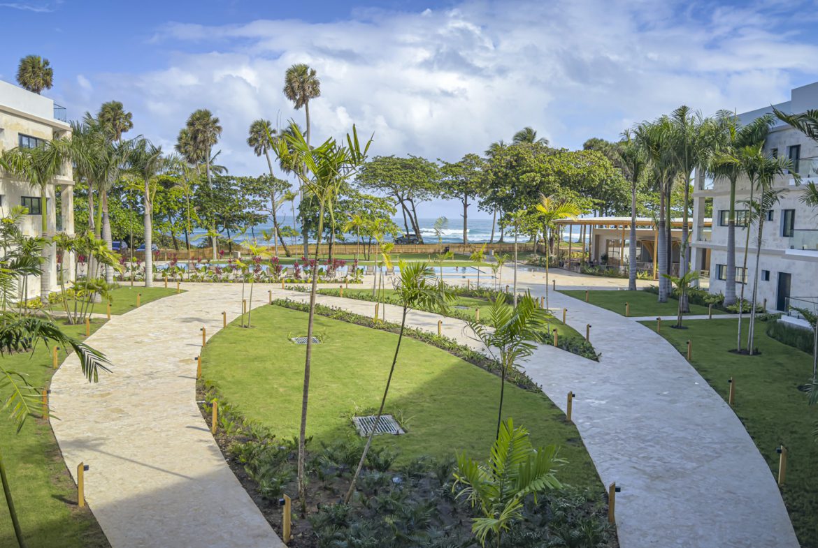 buyDRproperty Luxury resort courtyard with palm trees, walkways, and ocean view in the Dominican Republic. Sosua Real Estate