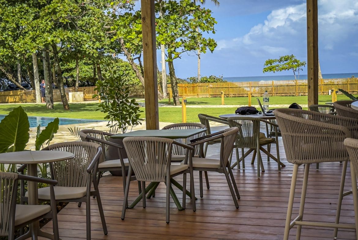 buyDRproperty Outdoor cafe with woven chairs overlooking a pool, lawn, and ocean view. Sosua Real Estate