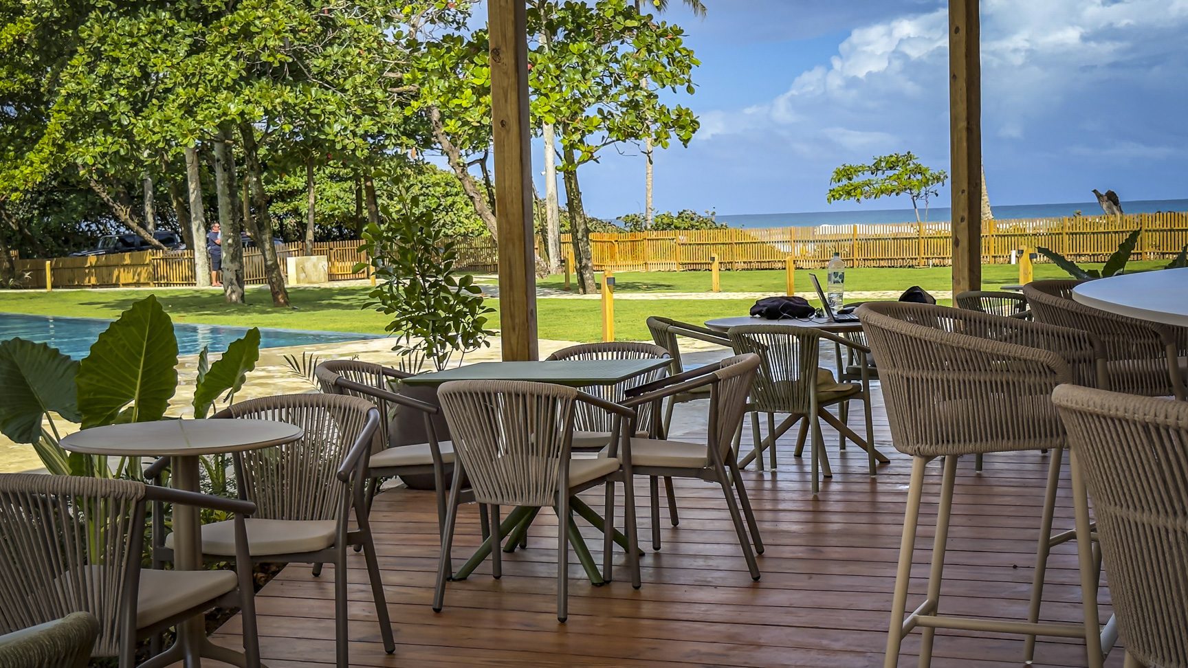 buyDRproperty Outdoor cafe with woven chairs overlooking a pool, lawn, and ocean view. Sosua Real Estate