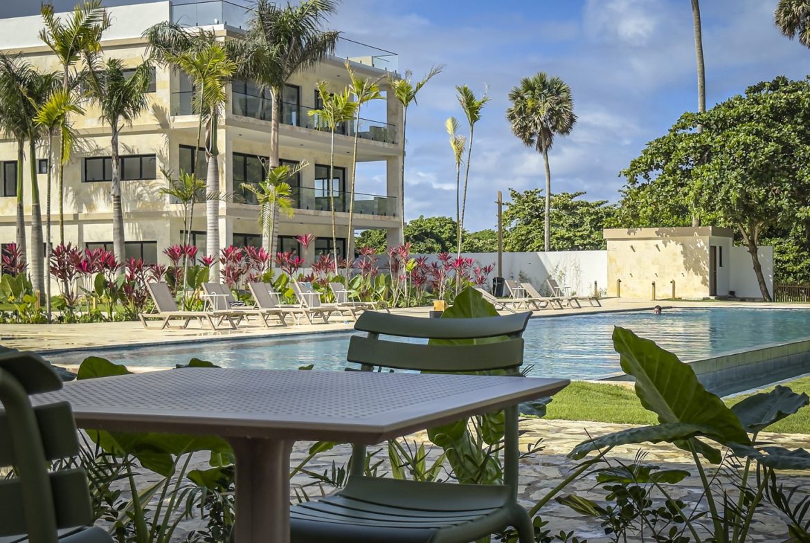 buyDRproperty Luxury resort pool with lounge chairs, palm trees, and modern building. Tropical vacation vibes. Sosua Real Estate