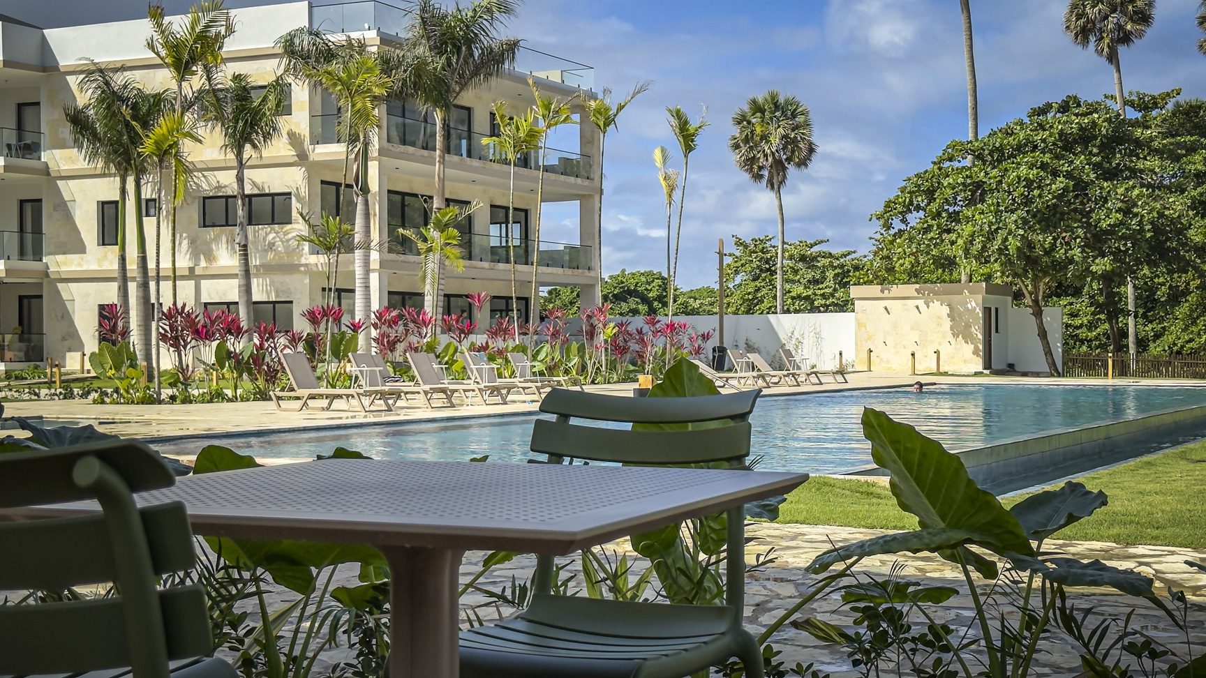 buyDRproperty Luxury resort pool with lounge chairs, palm trees, and modern building. Tropical vacation vibes. Sosua Real Estate