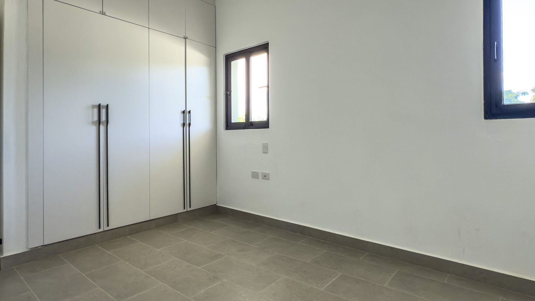 buyDRproperty Modern bedroom with built-in white wardrobe, gray tile floor, and black framed windows. Sosua Real Estate