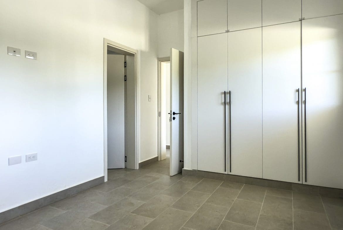 buyDRproperty Bright, modern bedroom with built-in white wardrobes and neutral tile flooring. Sosua Real Estate