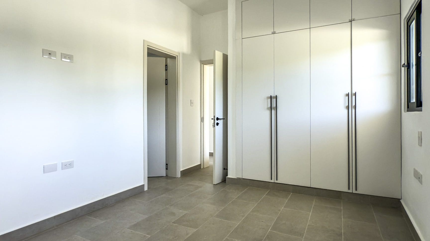 buyDRproperty Bright, modern bedroom with built-in white wardrobes and neutral tile flooring. Sosua Real Estate