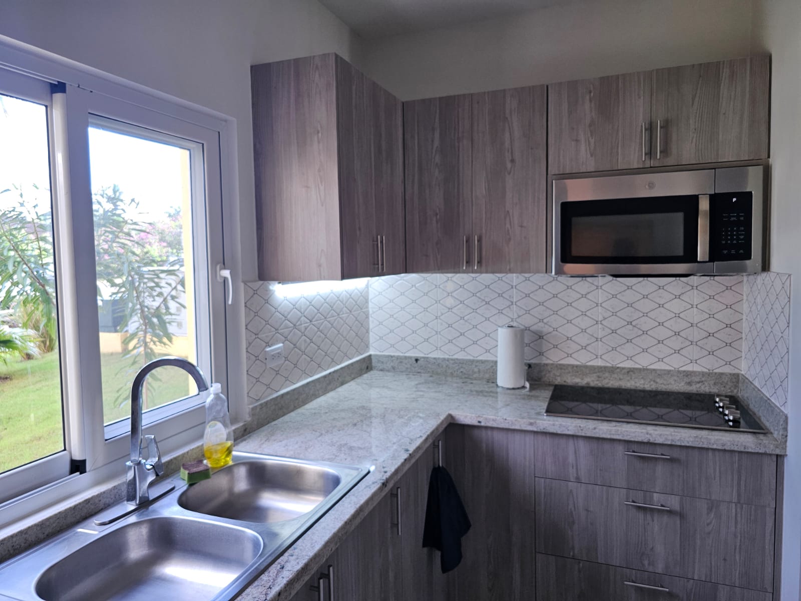 buyDRproperty Modern kitchen with stainless steel appliances, gray cabinets, granite countertops, and a large window. Sosua Real Estate