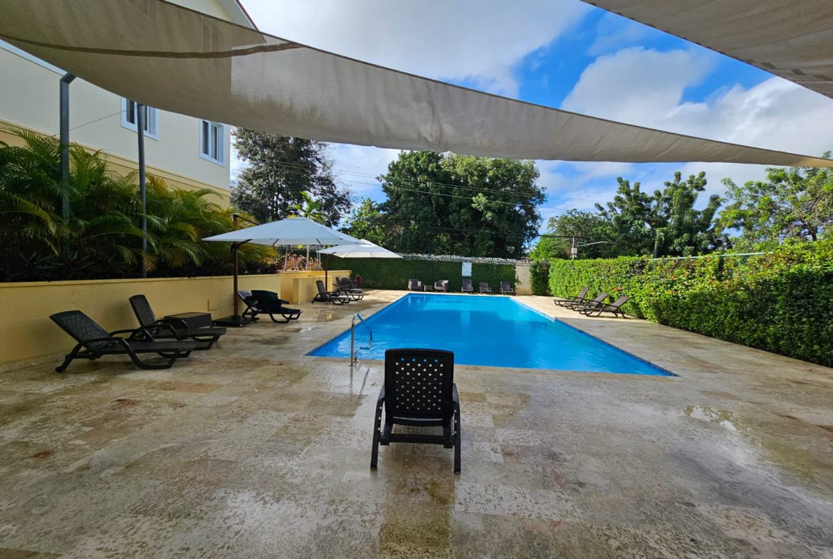 buyDRproperty Poolside relaxation: Lounge chairs surround a bright blue swimming pool under a shaded awning. Sosua Real Estate