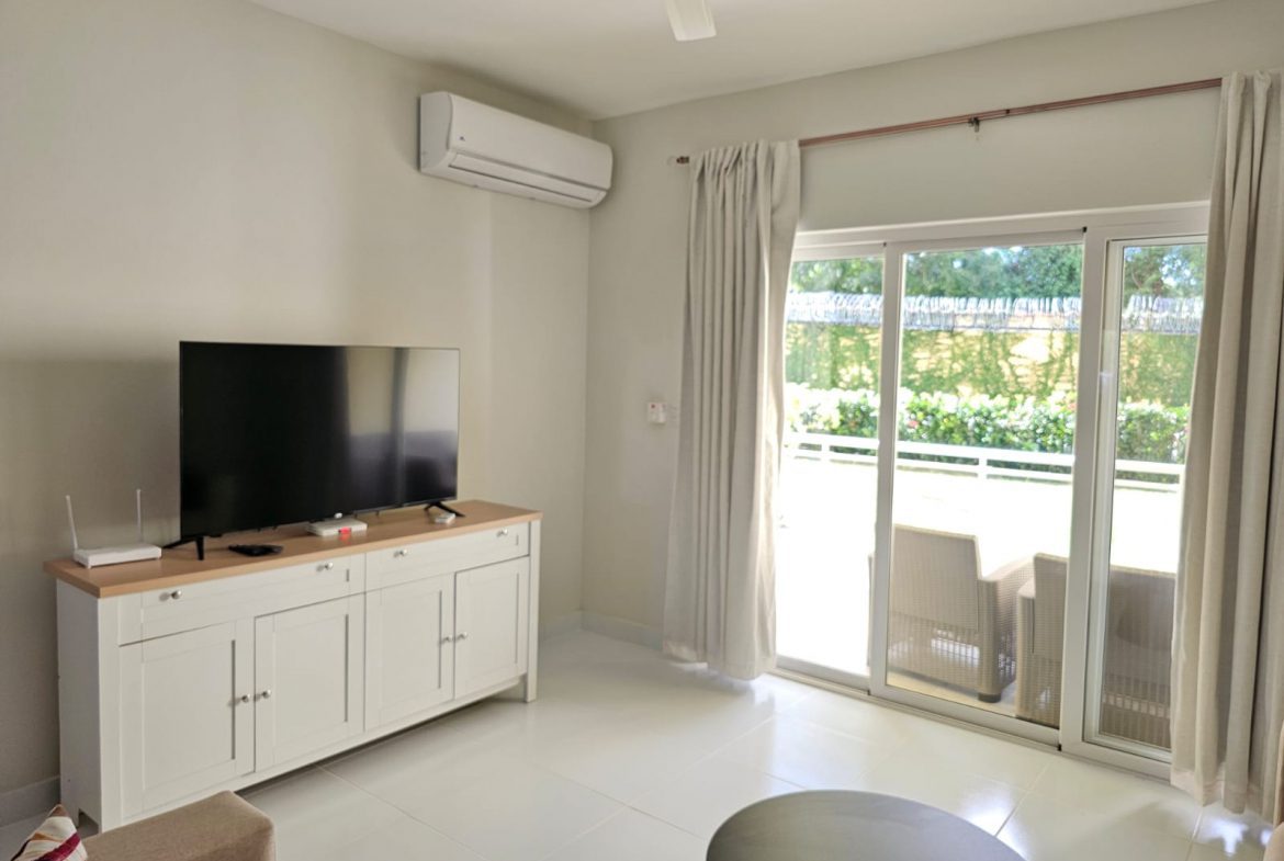 buyDRproperty Bright living room with white TV cabinet, air conditioner, and sliding glass doors to a patio. Sosua Real Estate