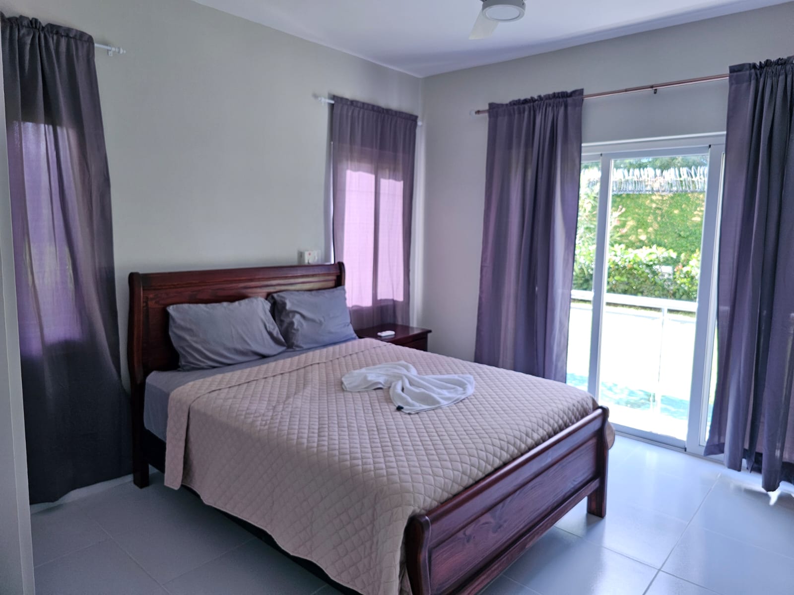 buyDRproperty Bedroom with a wooden bed, gray bedding, and purple curtains, leading to a balcony. Sosua Real Estate
