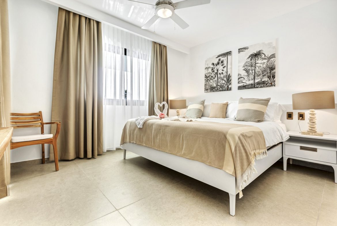 buyDRproperty Bright bedroom with white bed, beige accents, and tropical artwork above the headboard. Sosua Real Estate