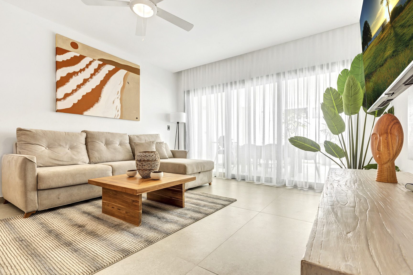 buyDRproperty Bright living room with beige sofa, modern art, and sheer curtains. Sosua Real Estate