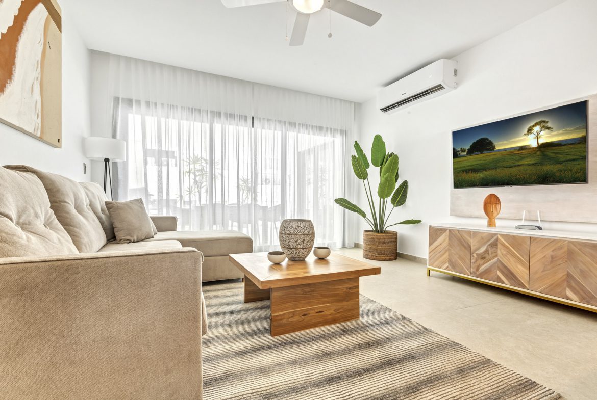 buyDRproperty Modern living room with beige sofa, wooden coffee table, TV, and indoor plant, creating a cozy and stylish interior. Sosua Real Estate