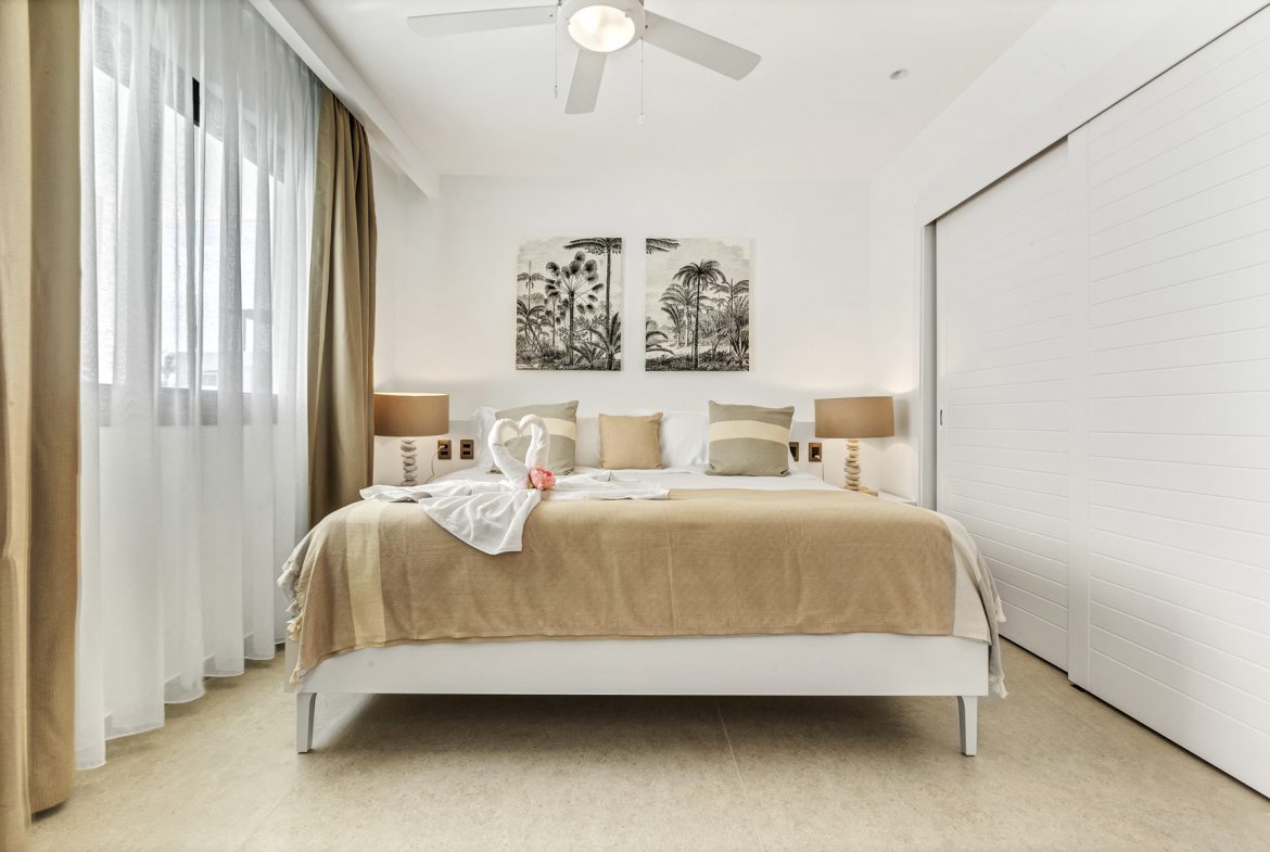 buyDRproperty Bright bedroom with king bed, palm tree art, and white linens. Modern coastal interior design. Sosua Real Estate