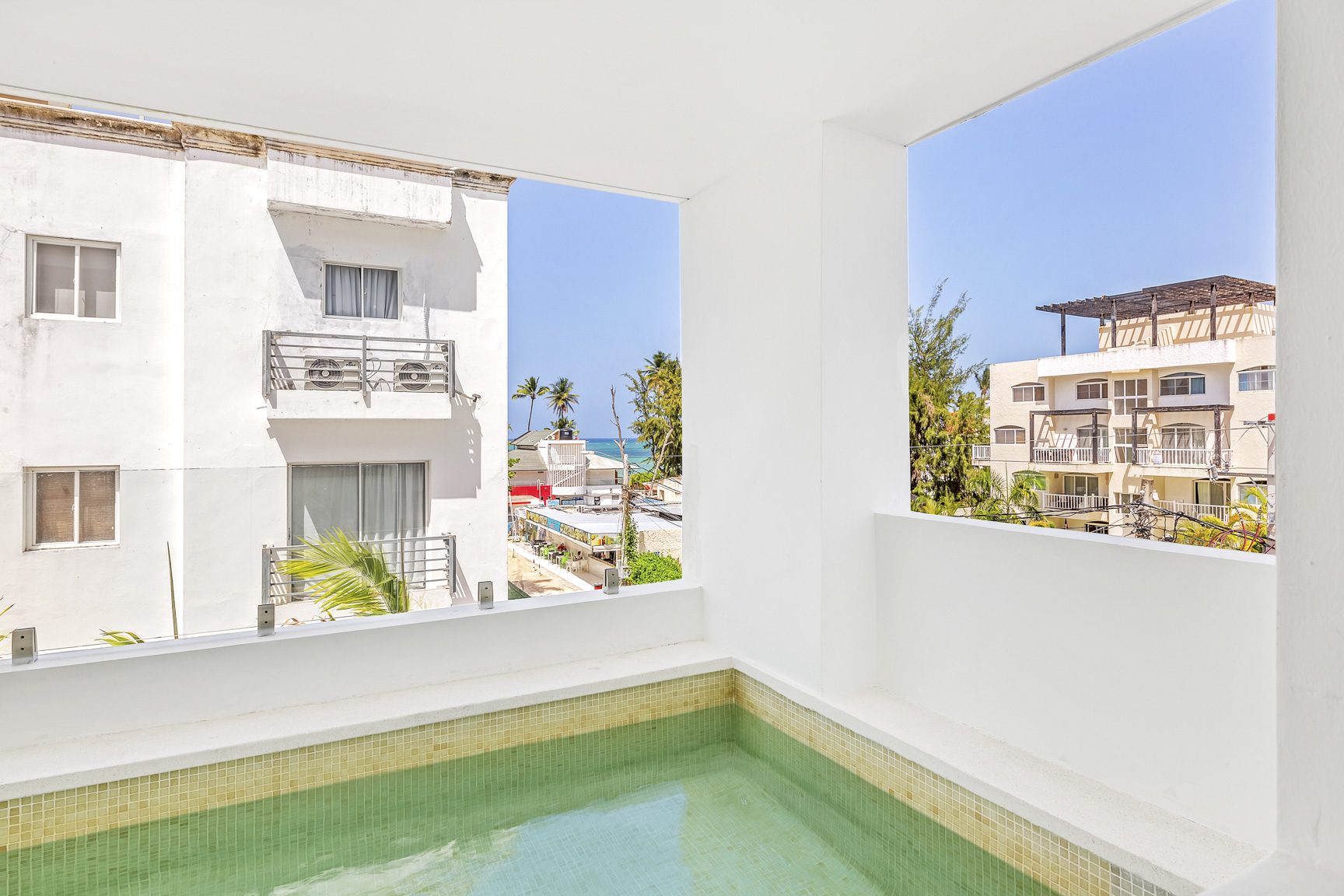 buyDRproperty Balcony view with a small pool overlooking tropical buildings and palm trees. Sosua Real Estate