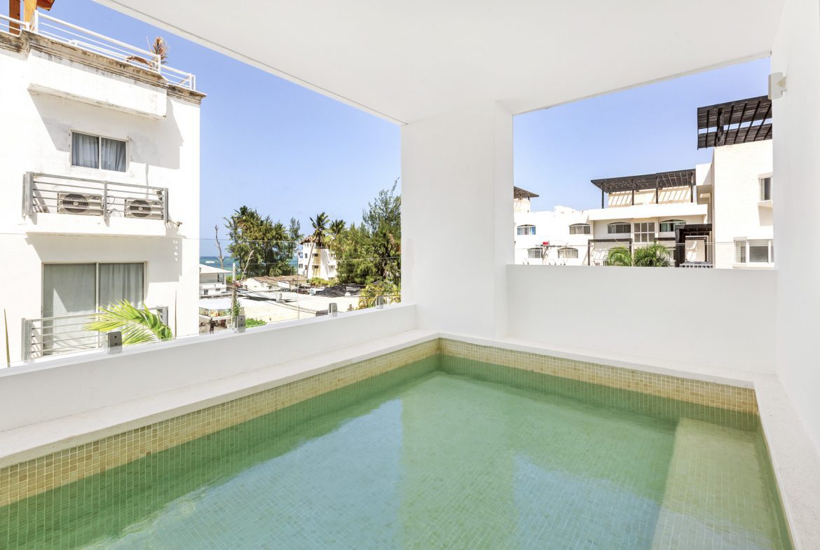 buyDRproperty Private rooftop pool with turquoise water overlooking buildings and palm trees on a sunny day. Sosua Real Estate