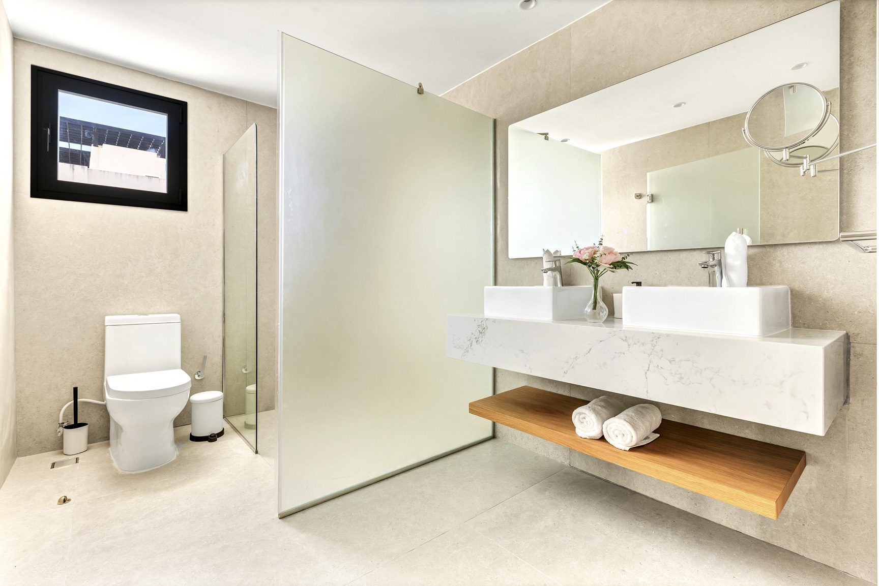 buyDRproperty Modern bathroom with double sinks, marble countertop, wood shelf, toilet, and glass shower screen. Sosua Real Estate