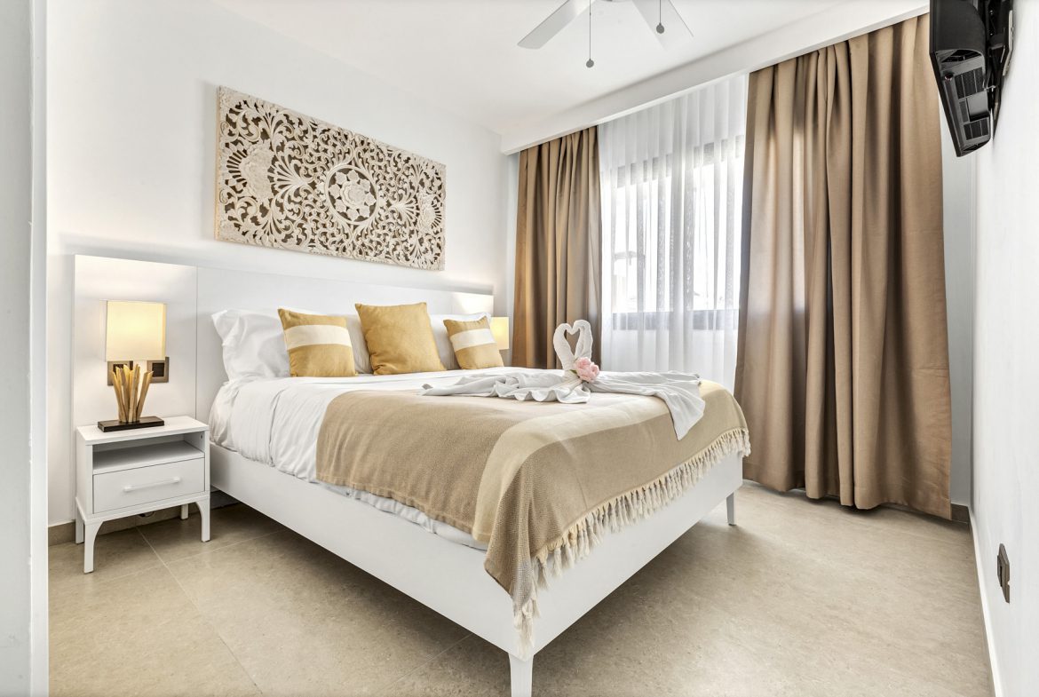 buyDRproperty Bright hotel room with white bed, gold accents, and carved wall art. Sosua Real Estate