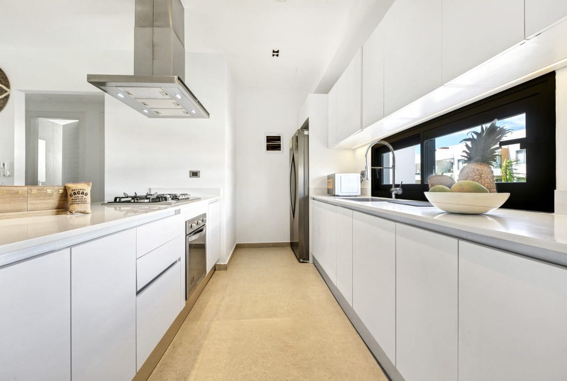 buyDRproperty Modern white kitchen with stainless steel appliances and a large window showing tropical foliage. Sosua Real Estate