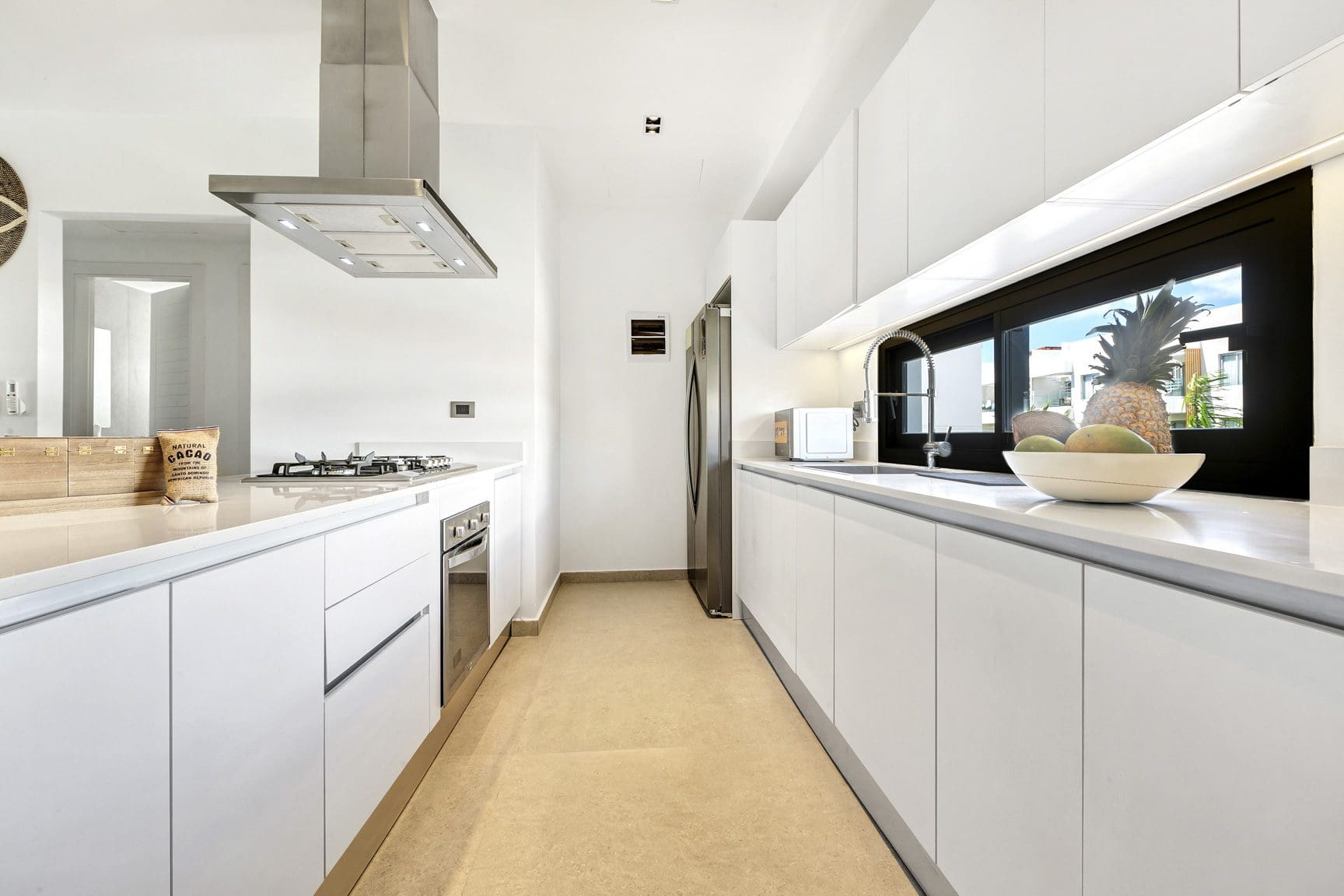 buyDRproperty Modern white kitchen with stainless steel appliances and a large window showing tropical foliage. Sosua Real Estate