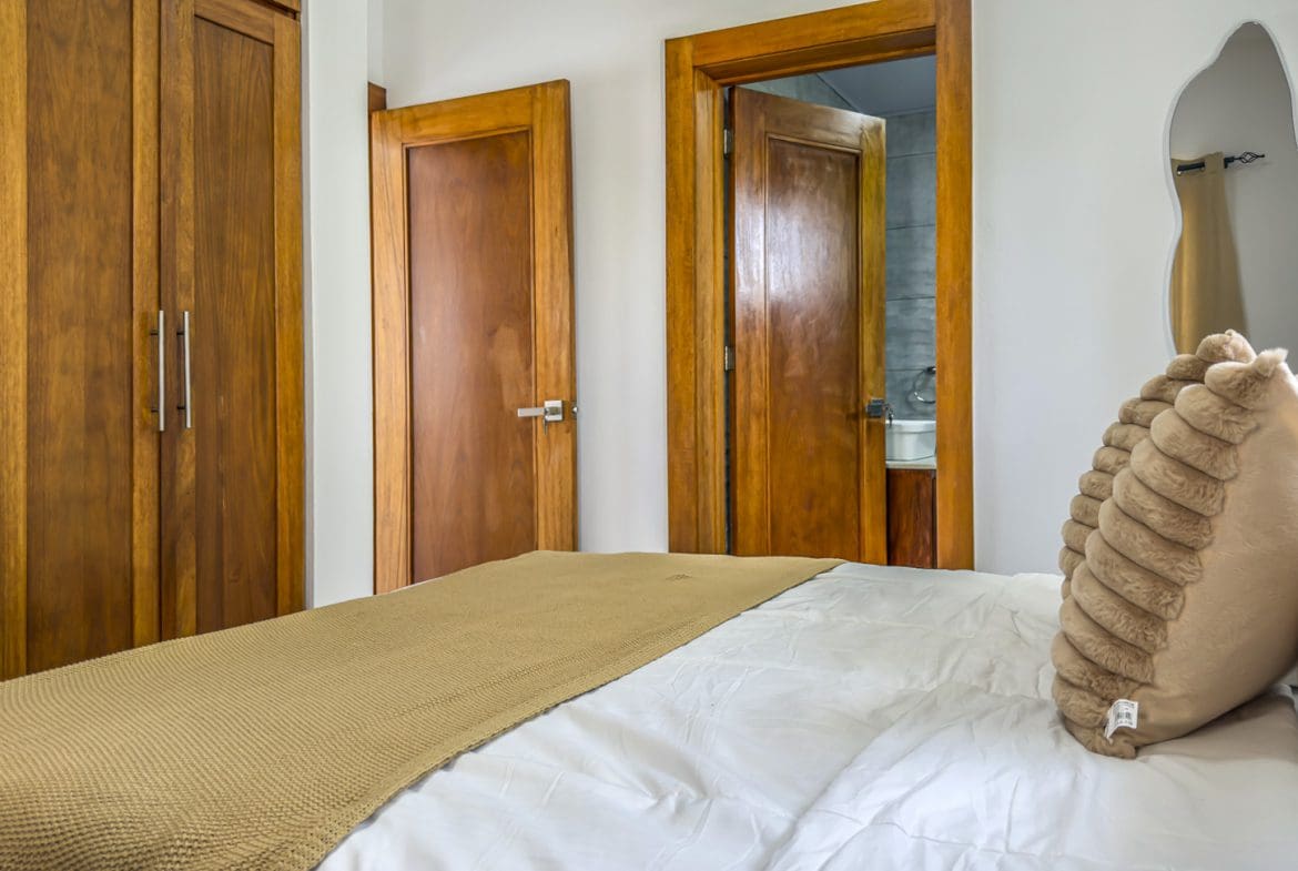 buyDRproperty Bedroom with wooden closet, door to bathroom, bed with white linens and tan throw blanket. Sosua Real Estate