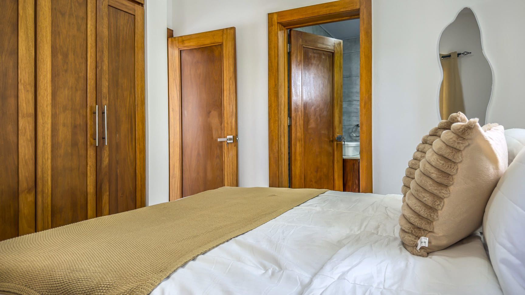 buyDRproperty Bedroom with wooden closet, door to bathroom, bed with white linens and tan throw blanket. Sosua Real Estate