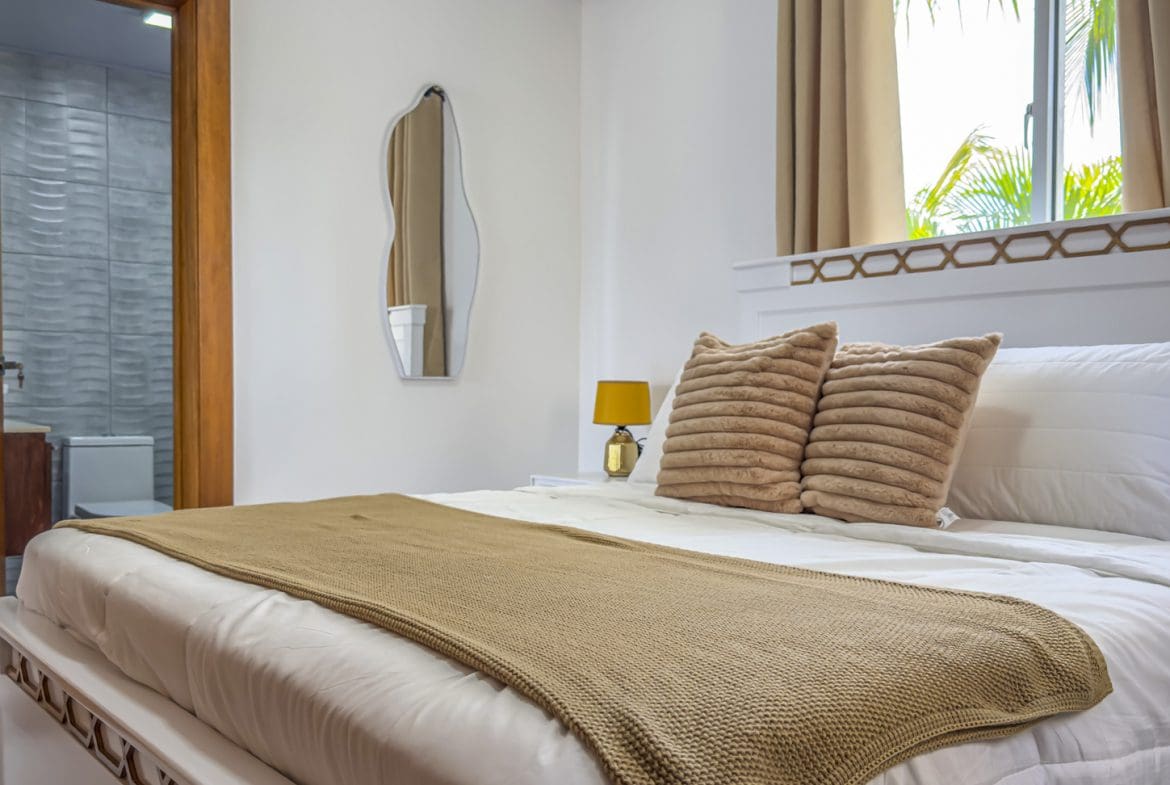 buyDRproperty Bright bedroom with white bedding, neutral accents, and bathroom access. Sosua Real Estate