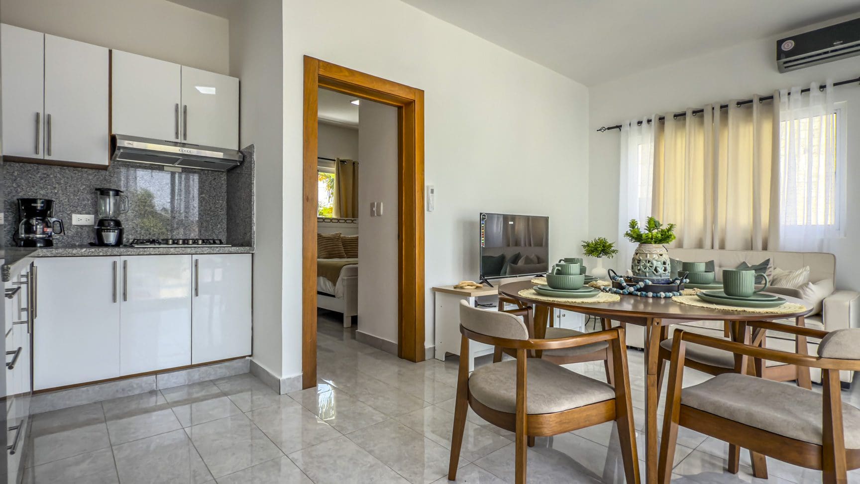 buyDRproperty Modern apartment interior with kitchen, dining area, living room, and bedroom visible through doorway. Sosua Real Estate
