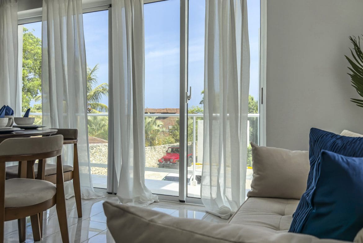 buyDRproperty Bright apartment interior with dining area, sheer curtains, and a view of a red car outside. Sosua Real Estate