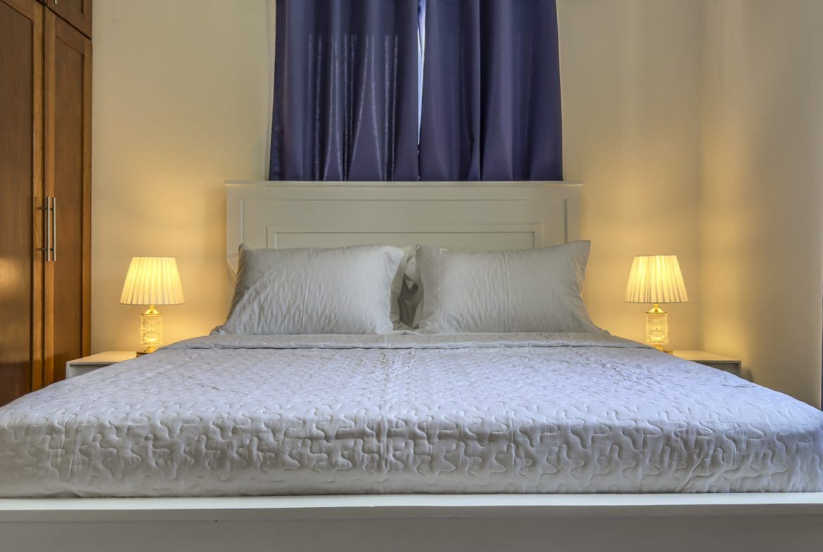 buyDRproperty Cozy small bedroom with white bed and warm lighting. Sosua Real Estate