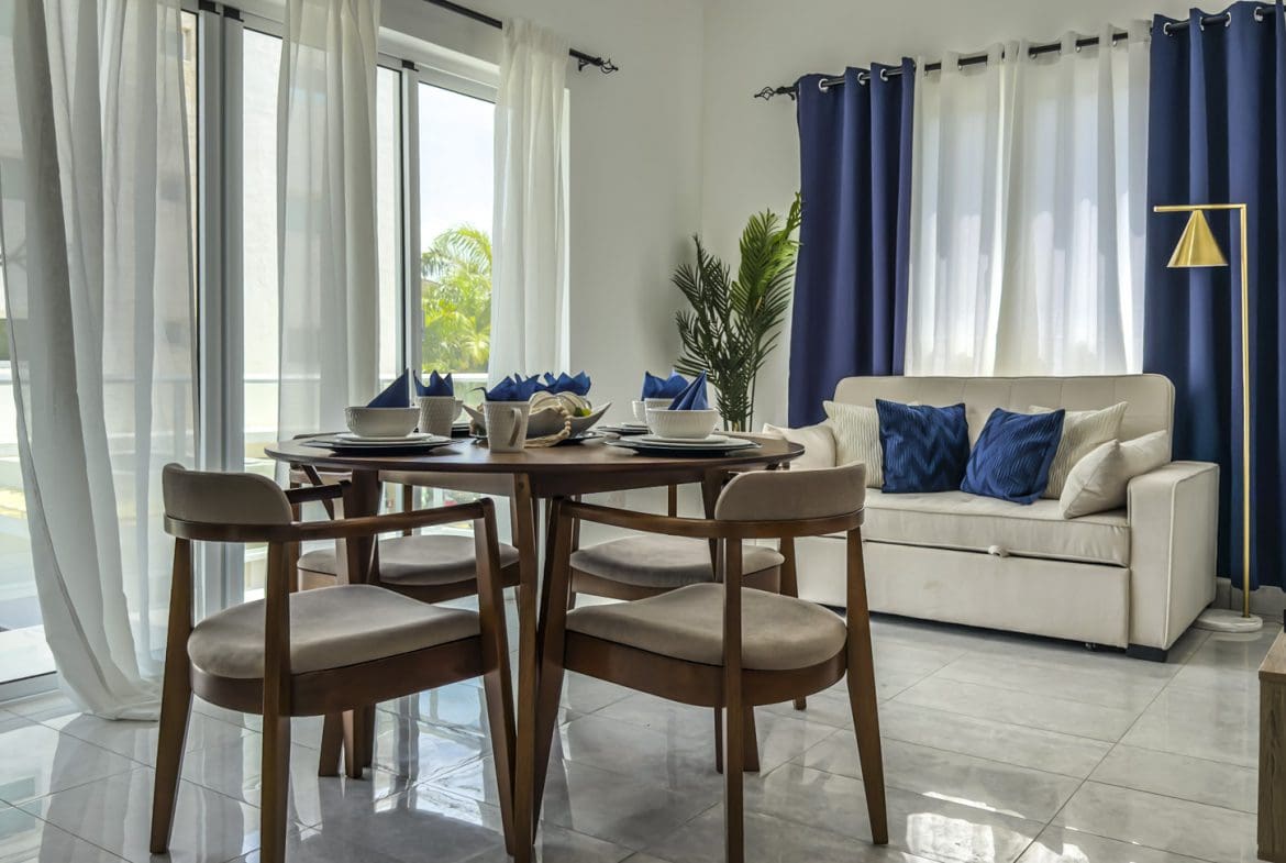 buyDRproperty Cozy dining area with round table, chairs, and sofa near window. Sosua Real Estate