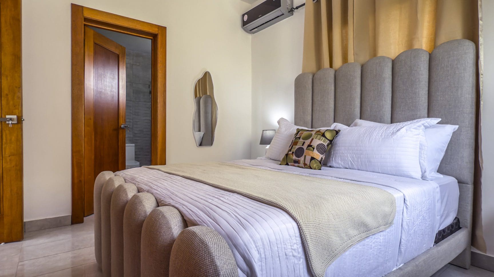 buyDRproperty Modern bedroom with a tufted headboard and footboard, open bathroom door, and minimalist decor. Sosua Real Estate