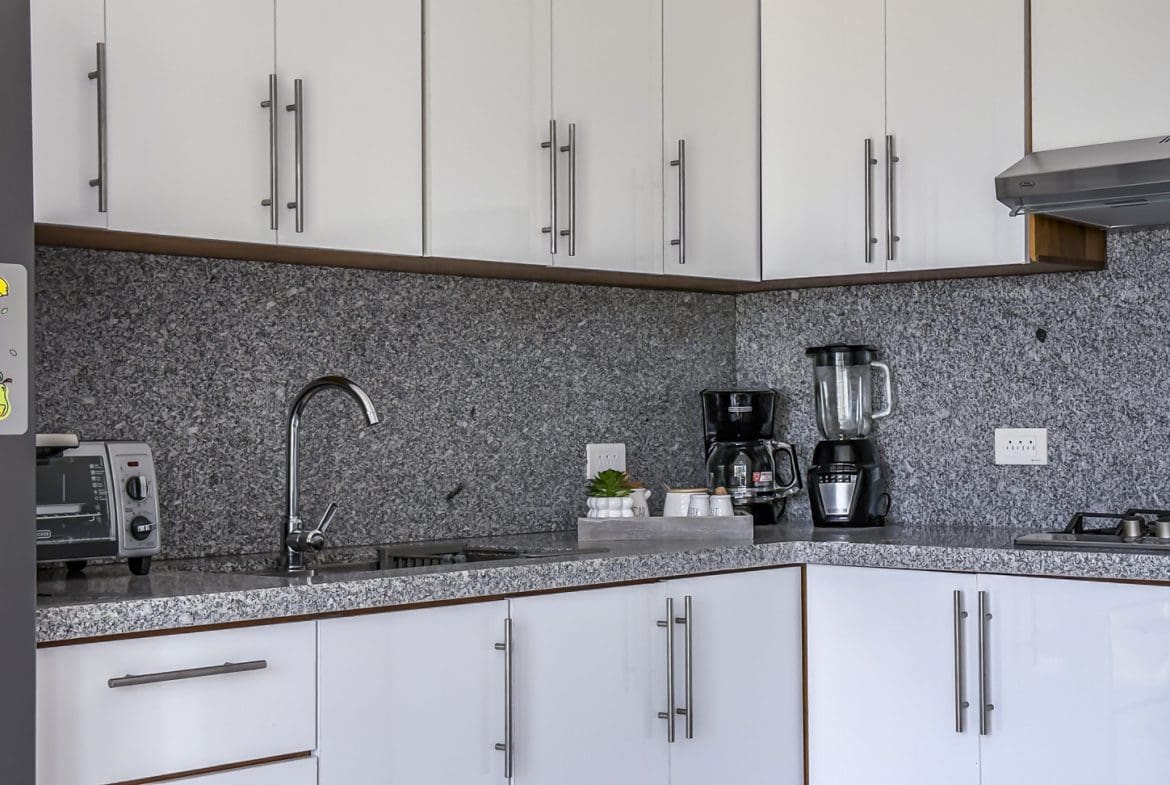 buyDRproperty Modern kitchen with white cabinets, granite countertops, stainless steel appliances, and a fruit sticker on the fridge. Sosua Real Estate