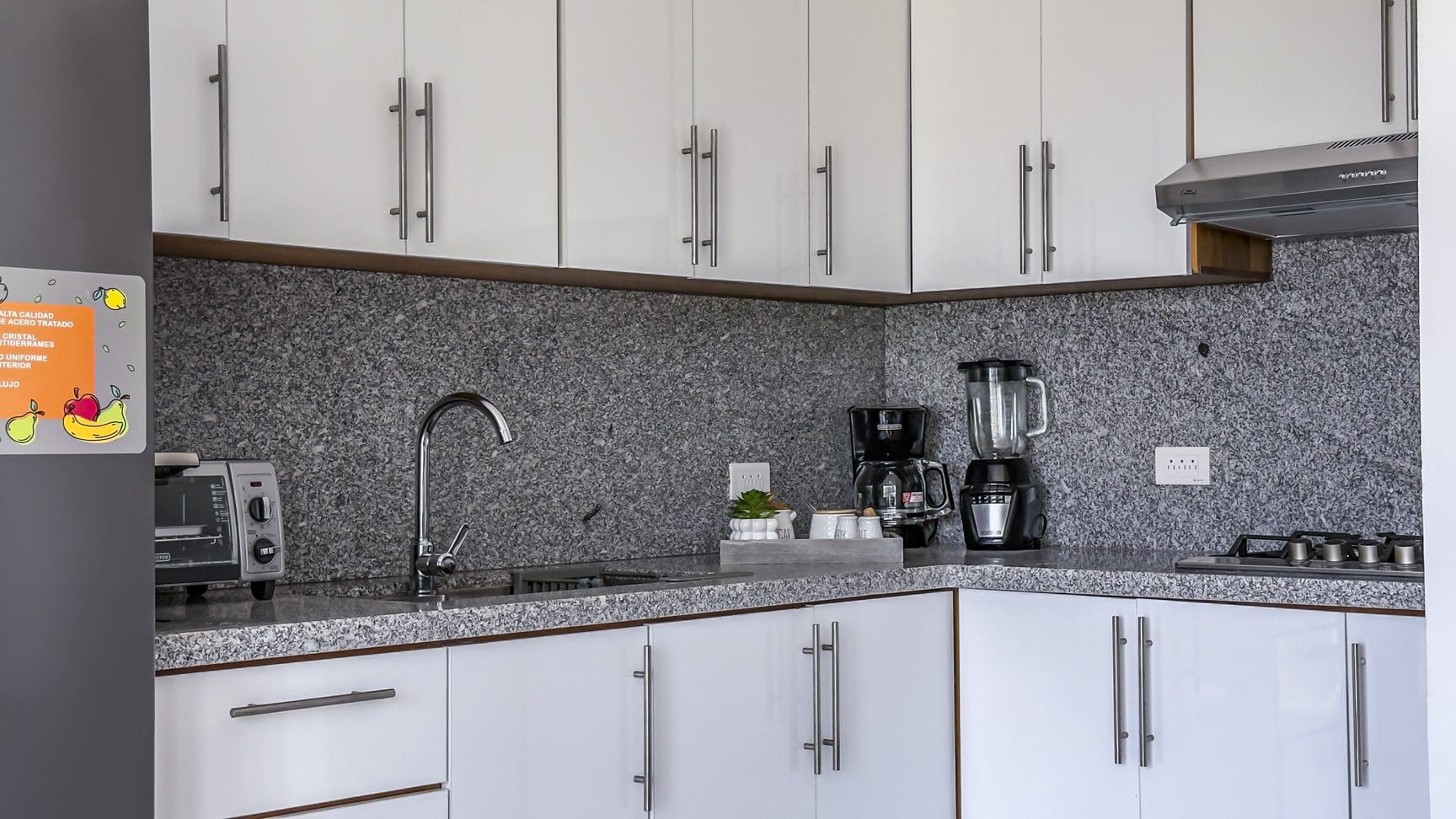 buyDRproperty Modern kitchen with white cabinets, granite countertops, stainless steel appliances, and a fruit sticker on the fridge. Sosua Real Estate