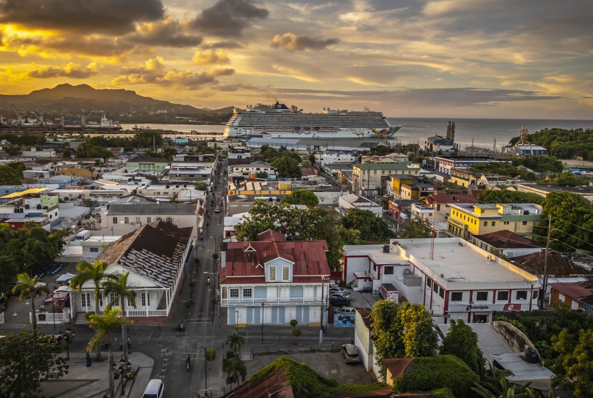buyDRproperty Puerto Plata cityscape at sunset with cruise ship in background. Colorful buildings and coastline view. Sosua Real Estate